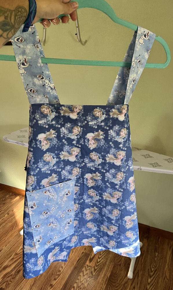 A child sized apron made from a base of Elsa fabric with olaf fabric details